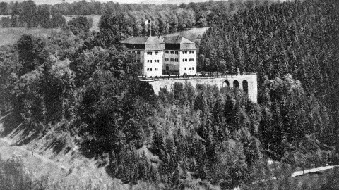 Panoramabild des Schlosses Grafeneck im Jahr 1930. Zu sehen ist das drei-flügelige Schloss auf einer Anhöhe, umgeben von Wald.